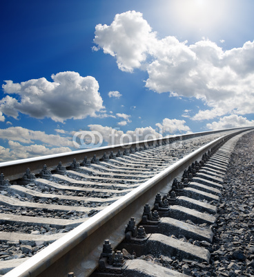 railway to horizon under cloudy sky with sun