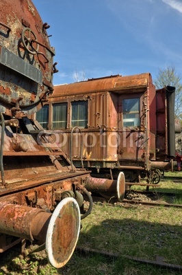 Corroded steam locomotive and railcar at train graveyard