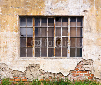 Large window with broken panes on dilapidated wall